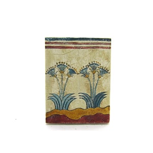 May include: A rectangular tile with a painted design of two blue papyrus plants with yellow flowers on a cream background. The tile has a red and blue border.