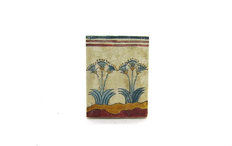 May include: A rectangular tile with a painted design of two blue papyrus plants with yellow flowers on a cream background. The tile has a red and blue border.