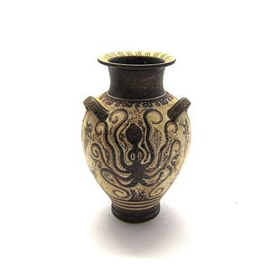 May include: A small, cream-coloured ceramic vase with a brown octopus design. The vase has two handles and a narrow neck.