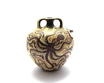 May include: A small, brown and cream ceramic vase with a design of an octopus in black and brown. The vase has two handles on the top.