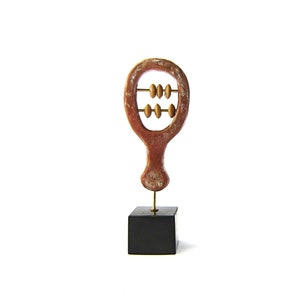 May include: A decorative abacus sculpture with a reddish-brown frame and golden beads. The abacus is mounted on a brass rod and a black square base. The background is plain white.