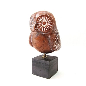 May include: A brown ceramic owl sculpture with white painted details, perched on a black wooden base.