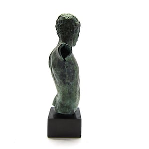 Pu&ograve; includere: Una scultura in bronzo di un torso maschile su una base nera. La scultura manca di un braccio e ha una patina verde.
