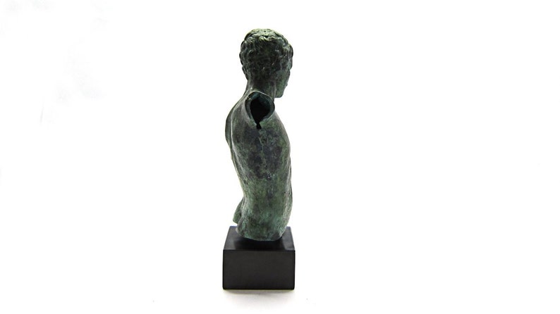 Pu&ograve; includere: Una scultura in bronzo di un torso maschile su una base nera. La scultura manca di un braccio e ha una patina verde.