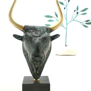 Op de afbeelding: Bronzen stierenkop sculptuur met gouden hoorns op een zwarte basis. Het beeldhouwwerk is een traditioneel Grieks ontwerp.