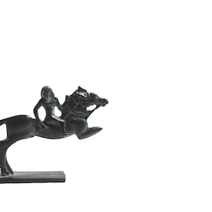 Può includere: Una statuetta in bronzo di una persona a cavallo, entrambi in posizione di salto. La statuetta è su una piccola base rettangolare.