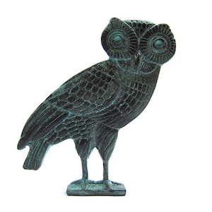 Puede incluir: Una pequeña estatua de bronce verde de un búho con plumas detalladas y grandes ojos. El búho está de pie sobre una base rectangular.