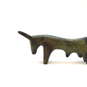 Könnte beinhalten: Eine stilisierte Bronzeskulptur eines Stiers mit grüner Patina, die auf einer weißen Oberfläche steht.