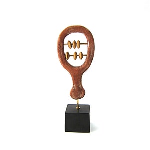 May include: A wooden abacus sculpture with a brown frame and gold beads. The abacus is mounted on a black square base. The sculpture is a decorative item.