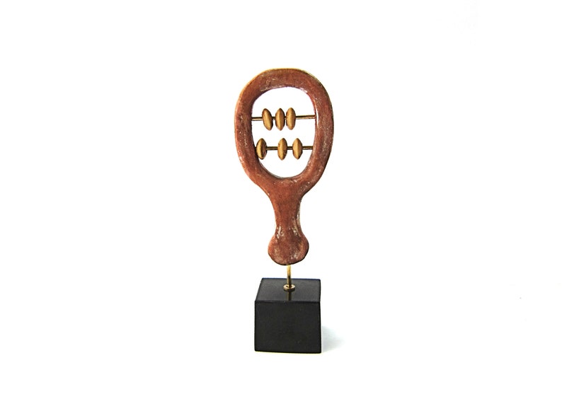 May include: A wooden abacus sculpture with a brown frame and gold beads. The abacus is mounted on a black square base. The sculpture is a decorative item.
