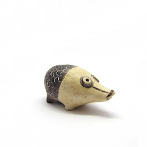 May include: A small ceramic sculpture of a pig with a brown and white patterned body and black eyes.