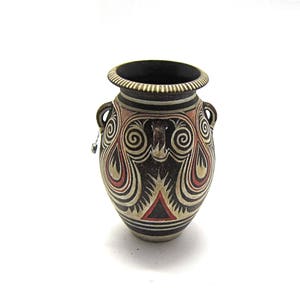 Puede incluir: Un jarrón de cerámica negro y blanco con diseños geométricos rojos y blancos. El jarrón tiene dos asas y un cuerpo redondo.
