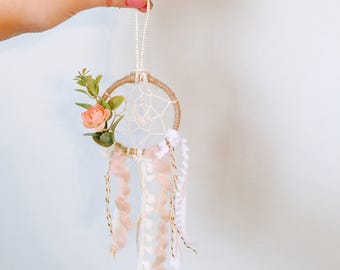May include: A small dream catcher with a white and brown macrame design, pink and white feathers, and a single pink flower.