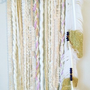 May include: A white, pink, and gold dream catcher with feathers and beads hanging from it.