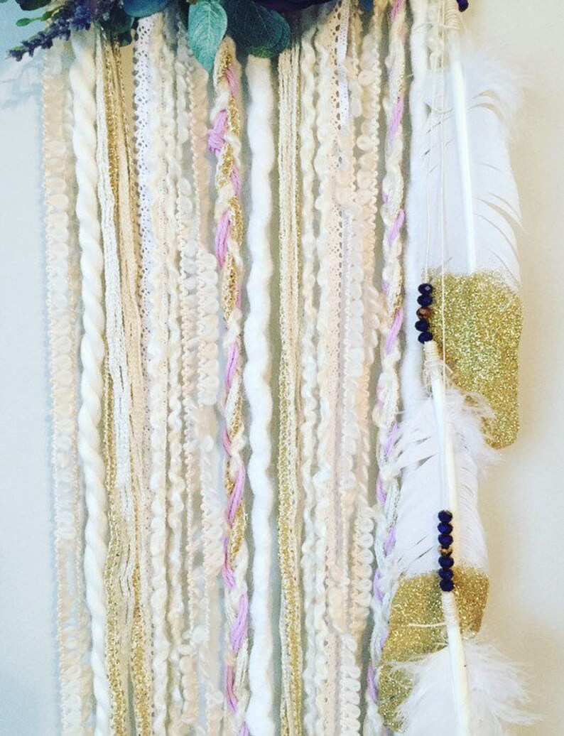 May include: A white, pink, and gold dream catcher with feathers and beads hanging from it.