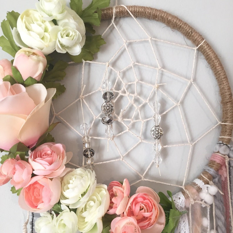 Puede incluir: Un atrapasue&ntilde;os blanco y beige con flecos de cuentas y una guirnalda floral de flores rosas y blancas.