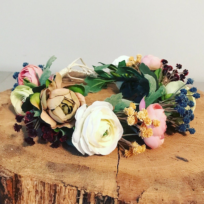 May include: A floral crown with white, pink, and brown flowers, green leaves, and blue berries.