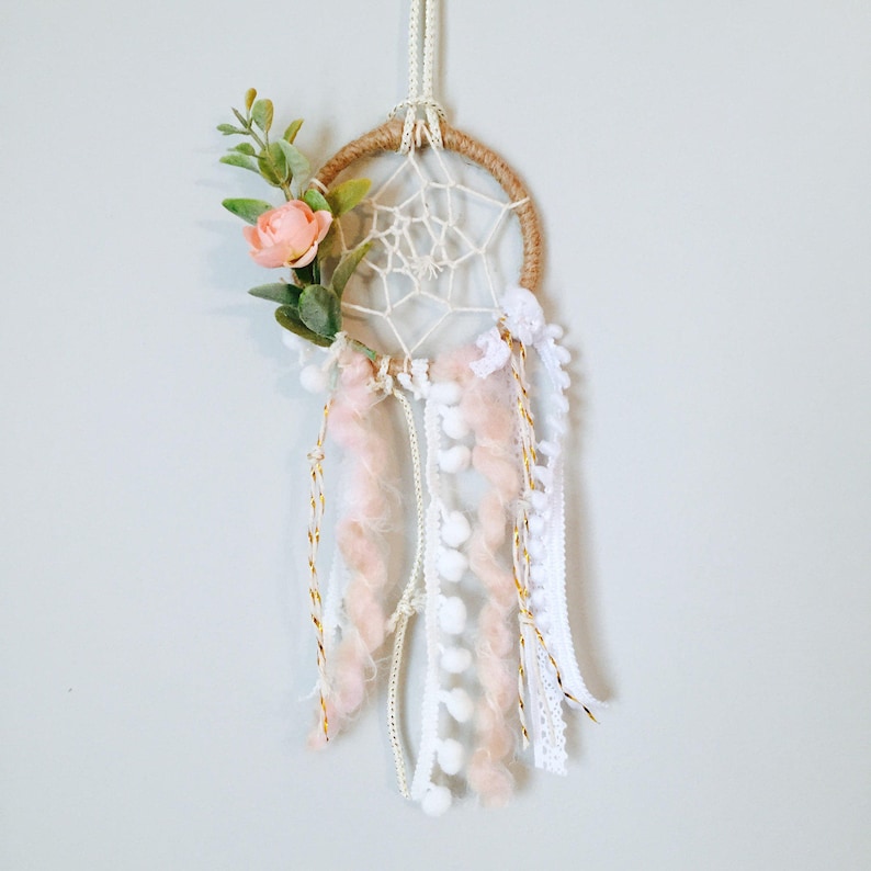 K&ouml;nnte beinhalten: Ein kleiner wei&szlig;er und rosa Traumf&auml;nger mit einem braunen Jute-Reifen, wei&szlig;en Federn und einer rosa Blume.