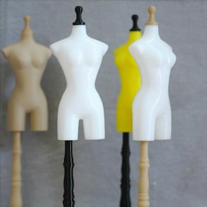 May include: Three different color mannequin torso forms on stands. The mannequins are white, tan, and yellow. The stands are black, tan, and black.