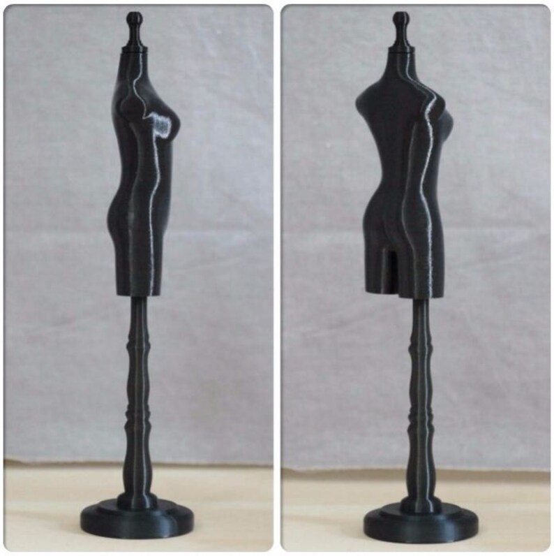 May include: A black plastic dress form with a stand. The dress form is a simple design with a rounded bust and a flat base. The stand is a simple design with a round base and a tall, slender column.
