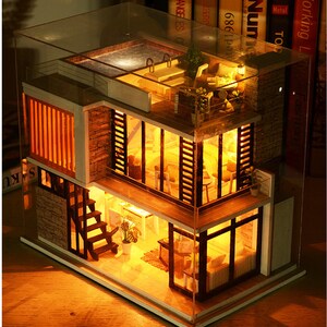 May include: A miniature dollhouse with a glass roof and a lit interior. The dollhouse has two levels, a rooftop pool, and a staircase. The dollhouse is made of wood and has a modern design.