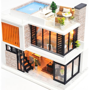 May include: A miniature dollhouse with a modern design, featuring a rooftop pool, a balcony with furniture, and a multi-level interior with windows and lights.