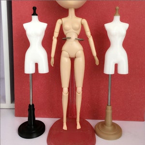 May include: Three doll-sized mannequins on stands. The mannequins are white plastic and have a feminine form. The stands are black, brown, and silver.