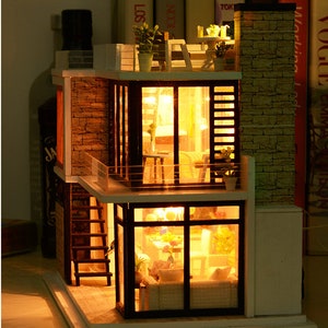 May include: A miniature wooden dollhouse with a modern design, featuring two levels, a balcony, and a brick exterior. The dollhouse is lit up with warm yellow lights, creating a cozy and inviting atmosphere.