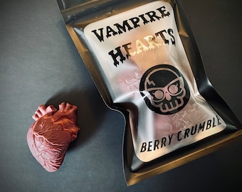 May include: A black and white bag with the text "Vampire Hearts Berry Crumble" printed on it. The bag is open and a red heart-shaped object is visible in the background.