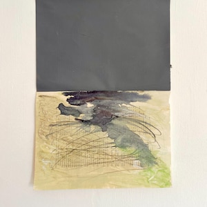 Könnte beinhalten: Abstraktes Kunstwerk mit schwarzem Hintergrund und einem strukturierten, beigefarbenen Papier mit schwarzen, grünen und blauen Aquarellspritzer.