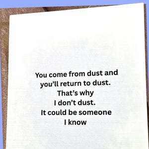 May include: A white greeting card with the text "You come from dust and you'll return to dust. That's why I don't dust. It could be someone I know" in black font. The card has a textured surface.