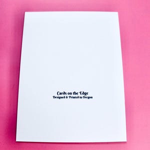 K&ouml;nnte beinhalten: Eine wei&szlig;e Gru&szlig;karte mit dem Text "Cards on the Edge Designed & Printed in Oregon" in Schwarz gedruckt. Die Karte befindet sich auf einem rosa Hintergrund.