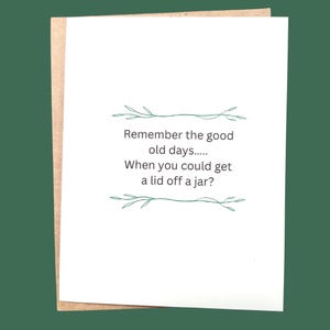 Könnte beinhalten: Eine weiße Grußkarte mit dem Text "Remember the good old days..... When you could get a lid off a jar?" in einer handschriftlichen Schriftart. Die Karte befindet sich auf einem braunen Umschlag mit grünem Hintergrund.