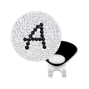 May include: A white golf ball with a black letter A made of rhinestones. The ball is attached to a silver golf ball marker with a black clip.