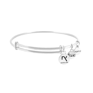 May include: Silver expandable bangle bracelet with three charms. The charms are round and feature the words "love", "inspired", and a symbol with the text "Navika Girl".