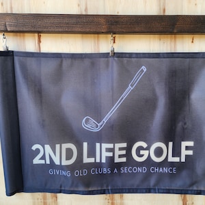 Puede incluir: Una pancarta negra con texto blanco que dice "2ND LIFE GOLF" y "GIVING OLD CLUBS A SECOND CHANCE". Un contorno blanco de un palo de golf está por encima del texto.