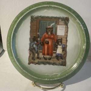 May include: A decorative plate with a green rim and a central illustration. The illustration depicts a family of bears in front of a schoolhouse. The bears are wearing clothes, and the plate is on a gold stand.