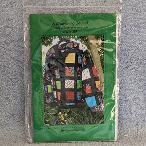May include: A green and white paper pattern packet with a colorful patchwork jacket design. The text on the packet reads "A Charm-ing Jacket using a sweatshirt as a base SWD 257 By Connie Spurlock".