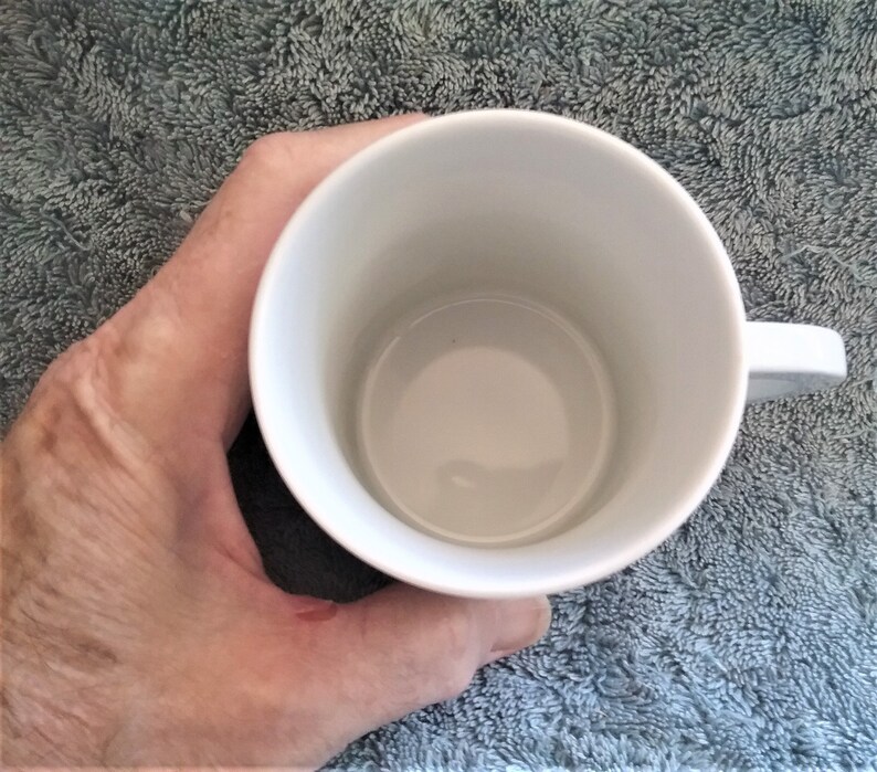 K&ouml;nnte beinhalten: Eine wei&szlig;e Keramiktasse mit Henkel. Die Tasse ist leer.