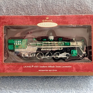 May include: A green and silver glass ornament of a Lionel 4501 Southern Mikado Steam Locomotive. The ornament is part of the Hallmark Keepsake Ornament Collection and the Crown Reflections des Fetes collection.