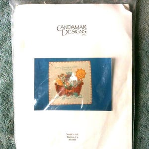 May include: A Candamar Designs Inc. cross-stitch kit in a clear plastic package. The kit includes a blue card with a stitched image of Noah's Ark, a sun, and the text "Every Spring is a Gift From God." The kit is labeled "Noah's Ark Button-Up #50955."