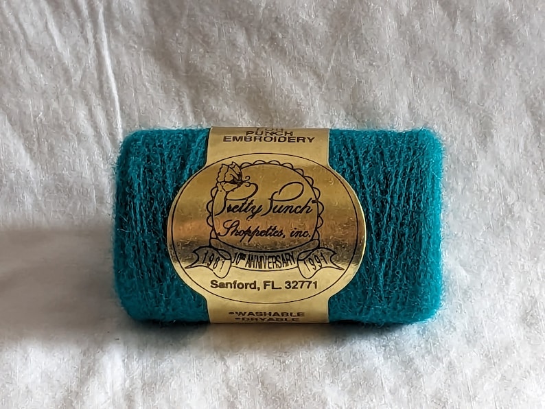 May include: A teal spool of embroidery floss with a gold label that reads "Pretty Punch Shoppettes, Inc. 1981 10th Anniversary 1991 Sanford, FL 32771 -Washable -Dryable"