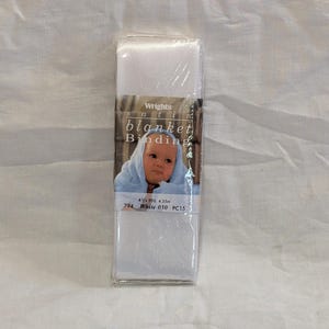 May include: A package of white satin blanket binding. The label features a baby wrapped in a blue blanket. The text on the label reads "Wrights satin blanket Binding", "4 1/2 YDS. 4.35m", "794 White 030 PC15".
