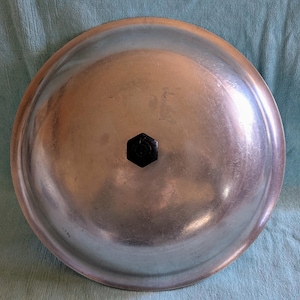 May include: Silver aluminum pot lid with a black knob in the center.