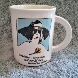 K&ouml;nnte beinhalten: Eine wei&szlig;e Keramiktasse mit einer Cartoon-Illustration einer Frau mit Sonnenbrille und einem gro&szlig;en Hut. Der Text auf der Tasse lautet "Listen honey - I say go ahead and wave at those Construction workers."