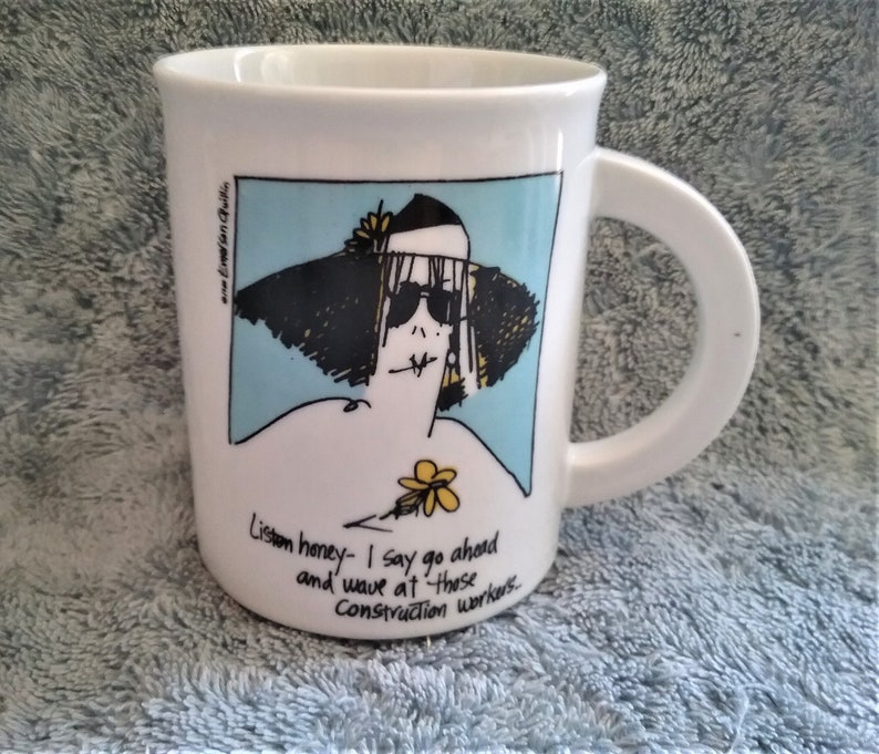 K&ouml;nnte beinhalten: Eine wei&szlig;e Keramiktasse mit einer Cartoon-Illustration einer Frau mit Sonnenbrille und einem gro&szlig;en Hut. Der Text auf der Tasse lautet "Listen honey - I say go ahead and wave at those Construction workers."