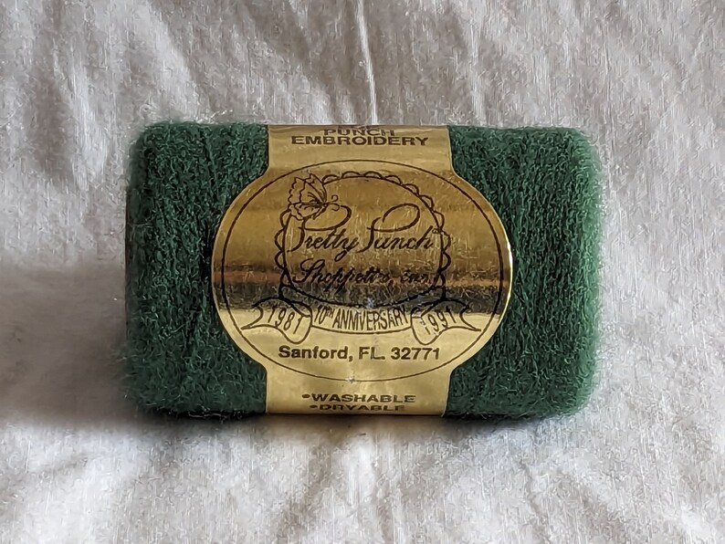 May include: A spool of green punch embroidery thread with a gold label that reads "Pretty Punch Shoppett's Inc. 1981 10th Anniversary 1991 Sanford, FL 32771 -Washable -Dryable"