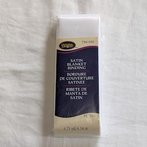 May include: A package of Wrights brand satin blanket binding. The label is dark blue with white text and gold accents. The package contains 4.75 yards of satin binding.