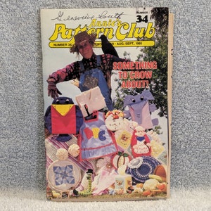 May include: A magazine cover for Annie's Pattern Club, issue number 34, August-September 1985. The cover features a scarecrow holding a variety of colorful handmade items, including a bird, an elephant, a bib, and a crocheted hat. The text on the cover reads "Something to Crow About!"