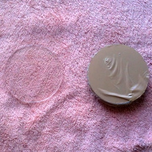 May include: A close-up of two round objects on a pink fuzzy surface. The object on the left is a clear glass circle. The object on the right is a brown circle with a textured surface.
